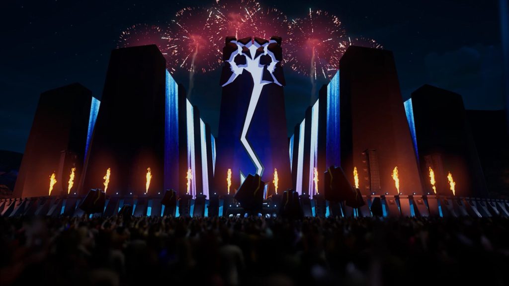 A dark stage with blue lights, pyrotechnics shooting off, and red fireworks above it