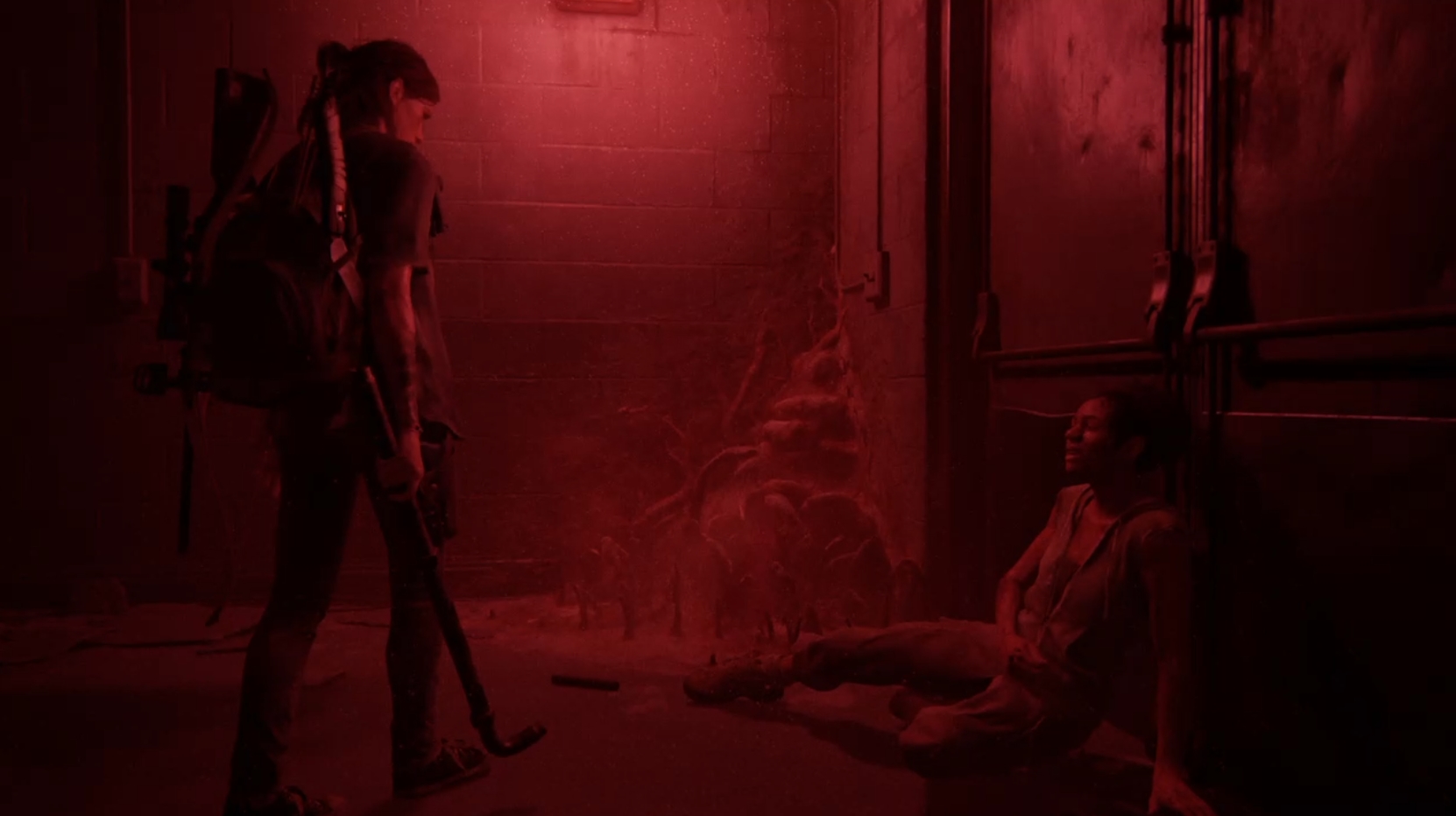 Ellie standing on the left over Nora who is on the ground on the right looking up at her. The lighting is all red.