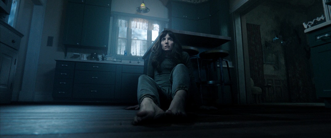 Maddison in Malignant looking terrified and backing up on the floor of her kitchen against the island